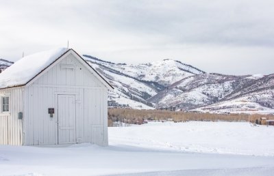 a-small-white-house-with-snow-covered-mountains-be-E8QSLK3