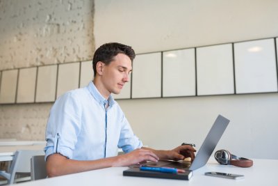 young handsome smiling man sitting in open space office working on laptop